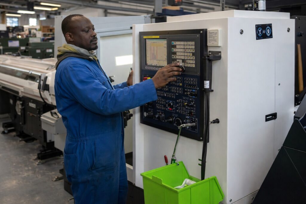 Factory worker operating CNC machine control panel in manufacturing facility