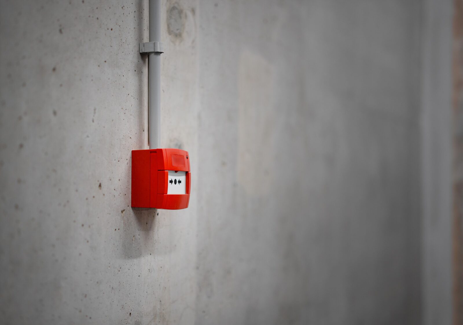 Red manual fire alarm call point mounted on a concrete wall